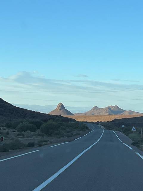       Road leading toward uniquely shaped desert peaks under clear sky.
  