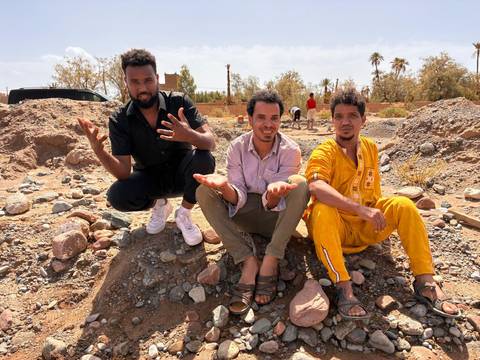       Same trio continue playful gestures on rocky ground in desert setting.
  
