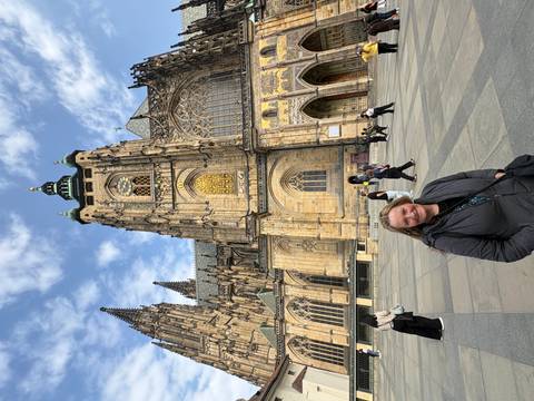       Smiling traveler standing in front of the gothic façade of St. Vitus Cathedral within Prague Castle complex.
  