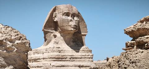       Close view of the weathered limestone Great Sphinx of Giza beneath a vivid blue sky.
  