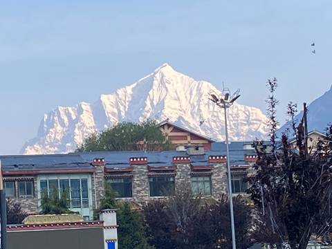       Distant snow-capped Himalayan peak rises above stone buildings and rooftops in early morning haze.
  