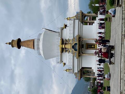       Large white chorten stupa with golden spire surrounded by worshippers circling the base in Bhutan.
  