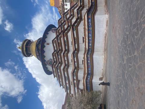       Tiered Gyantse Kumbum stupa with vibrant mural bands under a blue sky on the Tibetan Plateau.
  