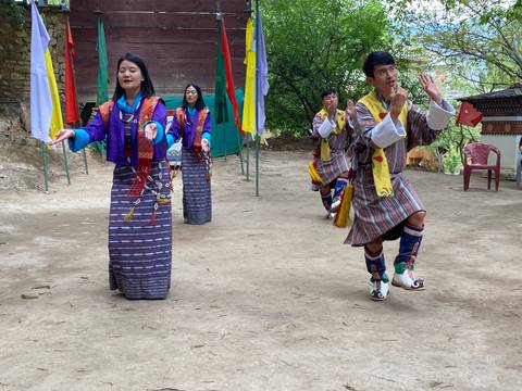       Bhutanese dancers in colorful traditional dress perform an outdoor folk dance with joyous expressions.
  