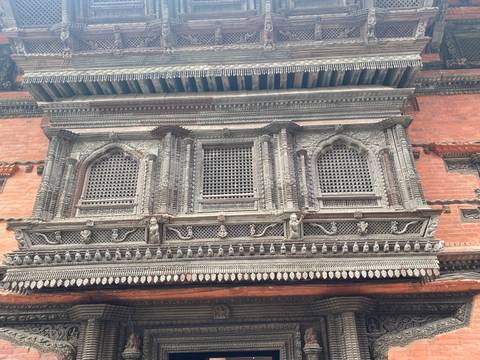      Close-up of intricately carved wooden window frame on a historic Newari brick building in Kathmandu.
  