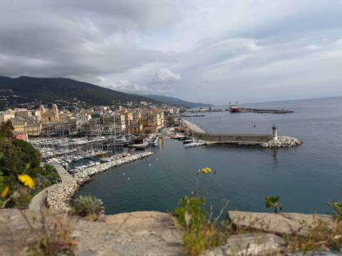       Harbor view of Bastia with pastel waterfront buildings, marina full of boats and surrounding hills.
  