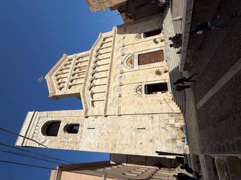       Cagliari Cathedral’s sandy-colored Romanesque façade and bell tower under a deep blue sky.
  