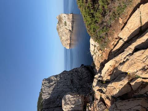       Sheer limestone cliffs framing a calm blue cove under a clear sky on Sardinia’s coast.
  