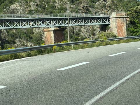       Close-up of a highway curve with metal guardrail and railway bridge in the background.
  