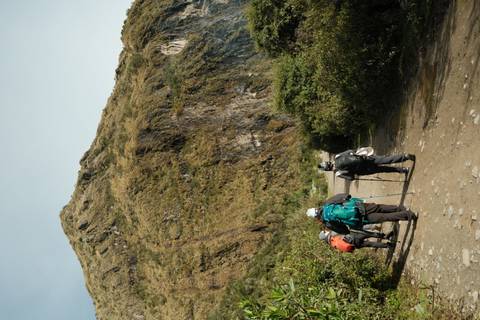       Back view of trekkers with backpacks and walking poles heading up a rugged Andean trail.
  