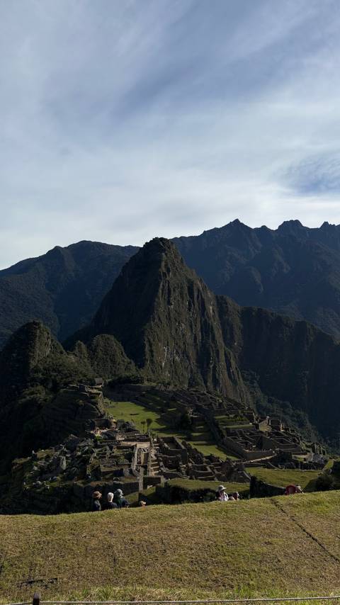       Iconic peak of Huayna Picchu rising sharply against a backdrop of dark ridged mountains.
  