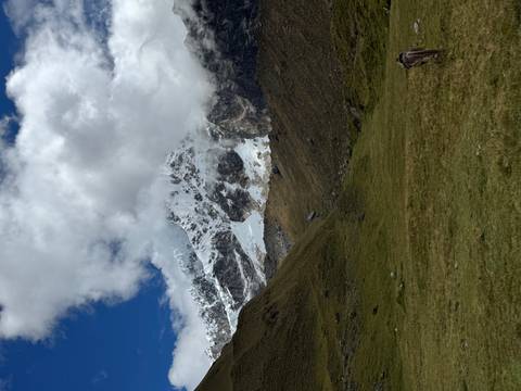       Snow-covered Andean peak emerging through clouds over a green valley.
  