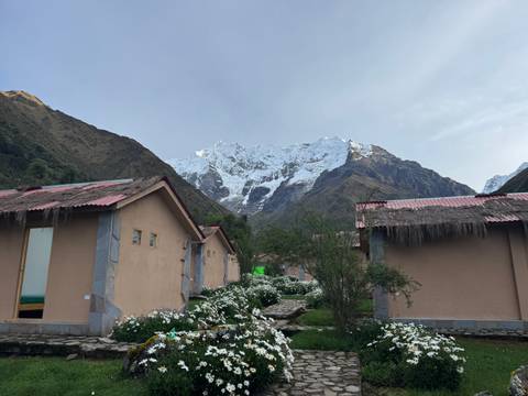       Mountain lodge huts surrounded by white flowers with a glacier-topped peak behind.
  