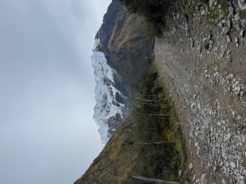       Rocky dirt road leading toward a snowy mountain ridge on an overcast day.
  