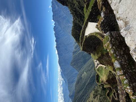       Stone Inca ruins perched on a ridge with sweeping views of green Andes under a striking sky.
  