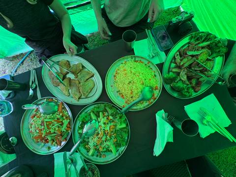       Table spread of colorful camp food dishes under a green expedition tent.
  