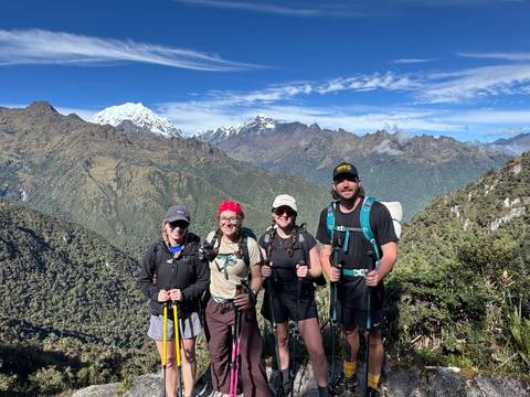       Four hikers posing on ridge with panoramic view of snow-topped Andes.
  