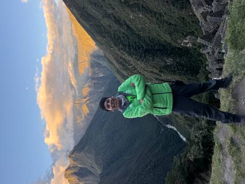       Guide in green jacket crossing arms against sunset-lit Andean valley.
  