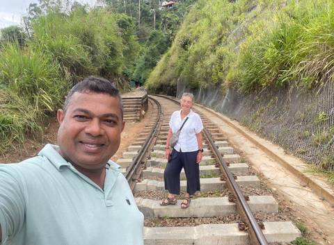       Guide and tourist pose on railway tracks cutting through lush hillside in Sri Lanka.
  