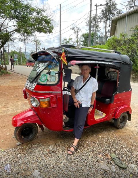       Tourist standing next to bright red tuk-tuk parked on rural roadside in Sri Lanka.
  