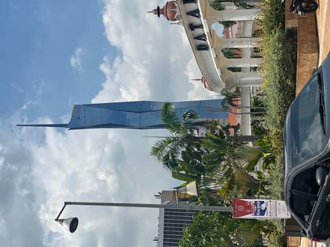       Daytime shot of the futuristic Merdeka 118 skyscraper rising above palm trees and city traffic.
  