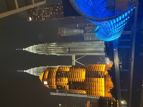       Kuala Lumpur night skyline with Petronas Towers, a golden-lit tower and the blue Saloma Link bridge.
  