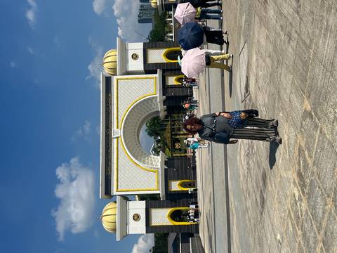       Tourist posing in front of the ornate yellow-domed royal palace gate under a bright blue sky.
  