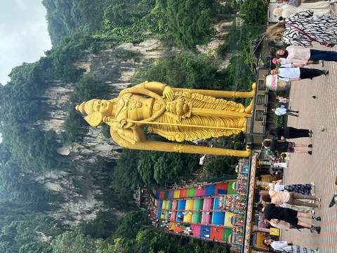       Huge golden statue of Lord Murugan at Batu Caves with rainbow staircase and crowds of visitors.
  