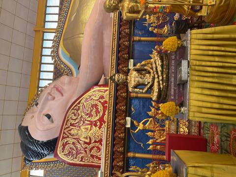       Temple interior showing reclining Buddha mural and gilded seated Buddha statues with offerings.
  
