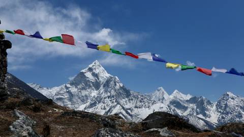       Colorful prayer flags fluttering in the foreground with a saw-toothed snowy Himalayan range behind.
  
