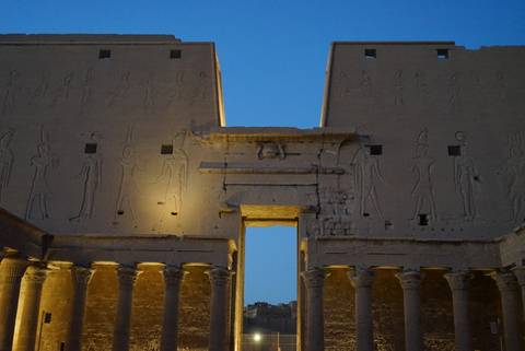       Nighttime illumination highlighting hieroglyph‐covered pylons and columns of an ancient Egyptian temple.
  