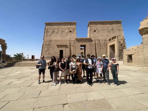       Tour group posing before carved reliefs at Philae Temple on a bright afternoon.
  