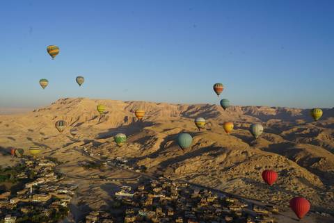       Dozens of colorful hot-air balloons drifting over the rugged desert mountains of Luxor at sunrise.
  