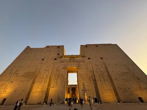       Twilight view looking up at the massive pylon entrance of Edfu Temple framed against a fading sky.
  