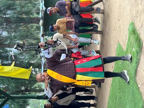       Bhutanese archer aiming a modern bow while spectators watch at an outdoor range.
  