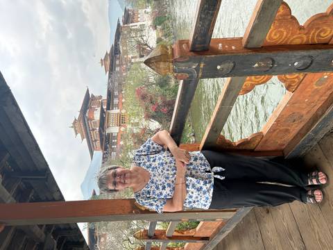       Visitor standing on a wooden bridge with the ornate Punakha Dzong and river behind.
  