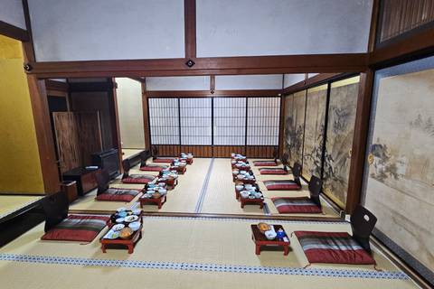       A traditional tatami room is set for a communal meal with low tables, cushions and neatly arranged dishes.
  