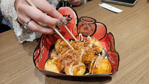       Close-up of takoyaki being lifted with chopsticks from a decorative paper tray.
  