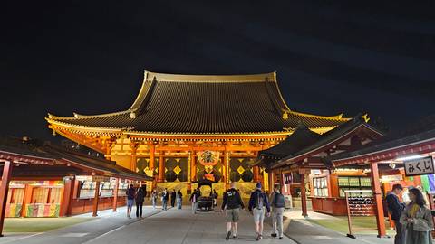       The illuminated main hall of Senso-ji temple glows richly at night as visitors stroll the courtyard.
  