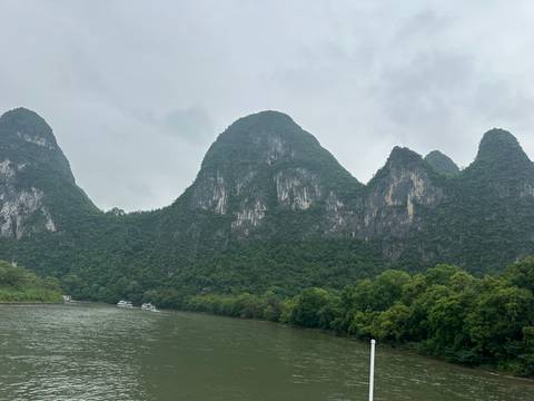       Steep karst peaks cloaked in dense forest rise sharply from a misty river in Guilin.
  