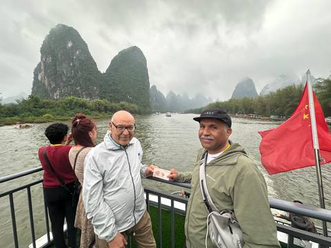       Tourists on a river boat pose with a Chinese banknote against the dramatic karst peaks of the Li River.
  