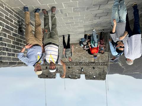       Smiling travelers celebrate atop a watchtower on the Great Wall, surrounded by mountainous terrain.
  