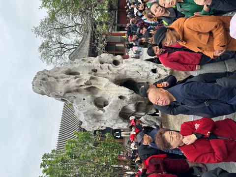       Large tour group gathered around an unusual eroded limestone rock in a traditional Chinese palace garden
  