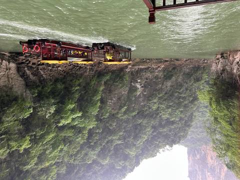       Twin red boats cruising through a dramatic narrow gorge with sheer rock walls and dense forest
  