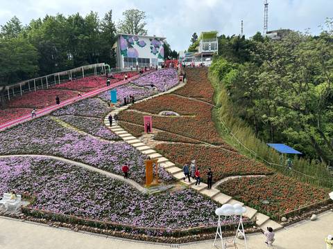       Colorful terraced flower garden on a hillside with winding stone paths and visitors walking
  