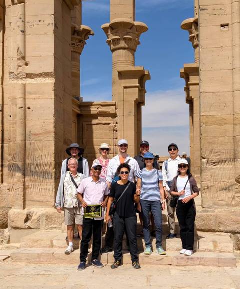       Group of tourists standing before ancient sandstone columns of an Egyptian temple.
  