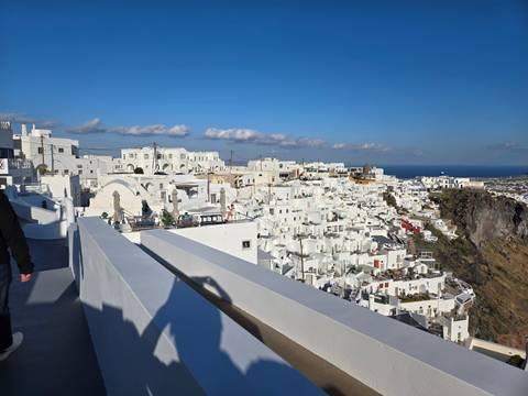       Bright white cube houses of Fira cascading down Santorini's caldera cliffs under a clear sky.
  