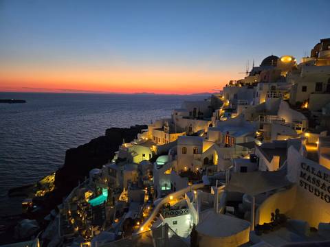       Iconic village of Oia illuminated at dusk with white houses and blue domes cascading down the cliff.
  