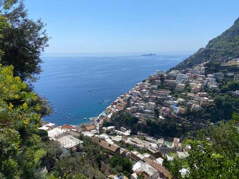       High vantage view of colorful Positano cascading down steep cliffs to the blue Tyrrhenian Sea dotted with boats
  