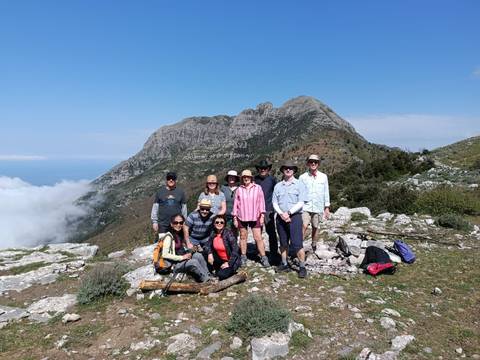       Happy hiking group posing on a rocky ridge with dramatic coastal mountains and low clouds behind
  